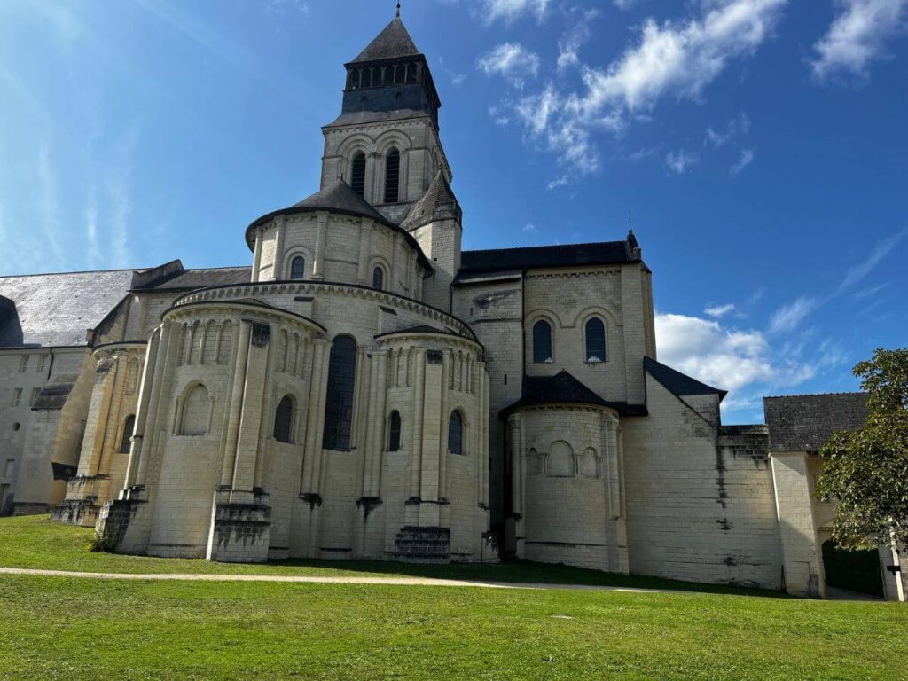 The Royal Abbey at Fontevraud from the outside with green grass in front and a blue sky with a couple of clouds behind