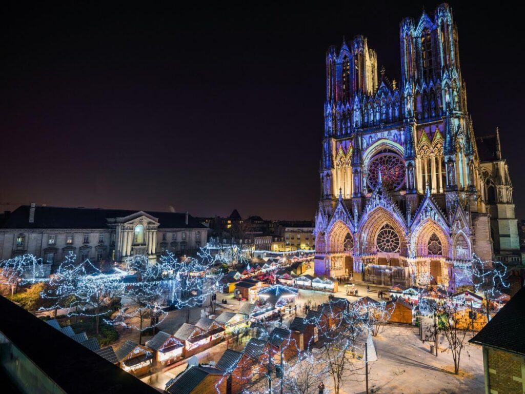 A cathedral lit up with a christmas market set up in front of it at night
