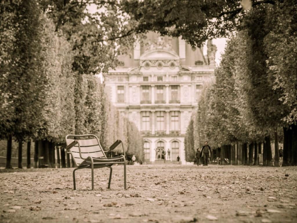 A black and white old photo of the Tuileries with an empty cafe chair sat to one side in a spooky way