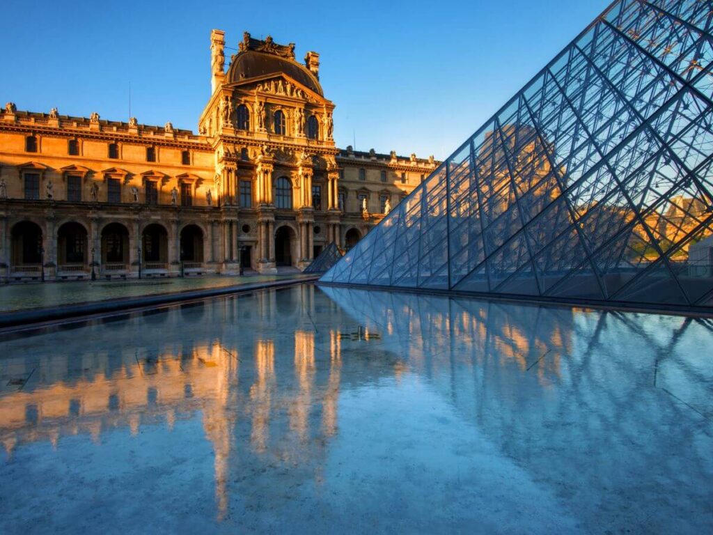 The Louvre in the late afternoon with water shining on the floor and a blue sky