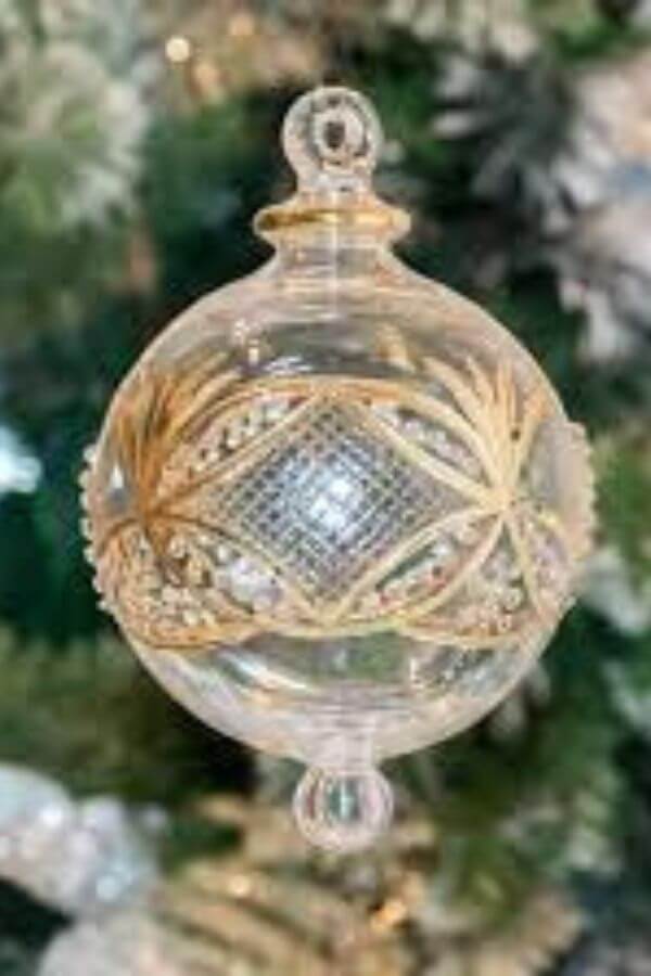 A see through glass Christmass bauble with gold on it hanging from a Christmas Tree