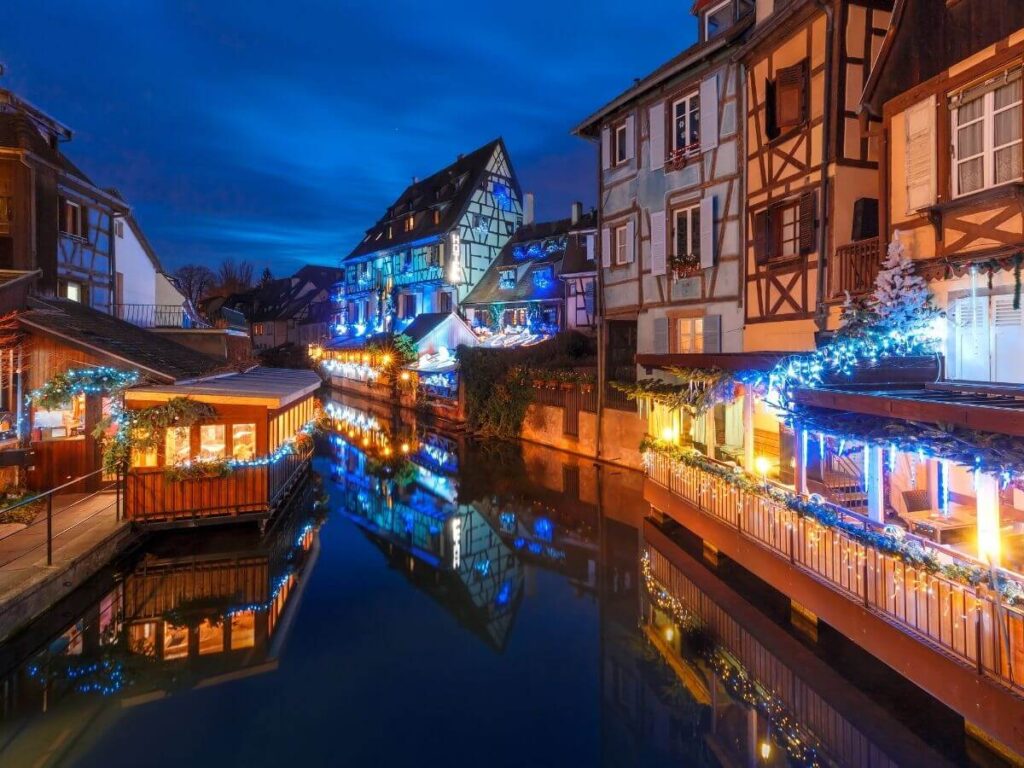 An evening Christmas scene outside in a French village with a river running through it and old half-timbered buildings either side