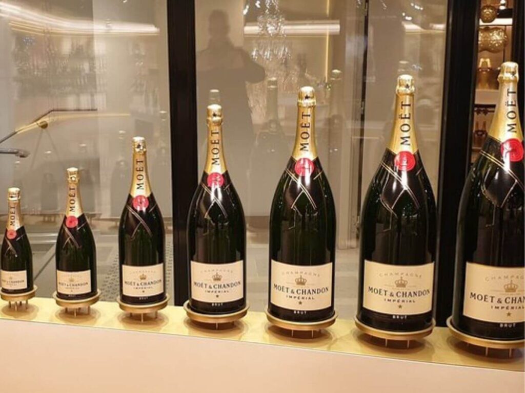 Bottles of Moet and Chandon champagne going down in size sat in front of some glass on a light coloured stone