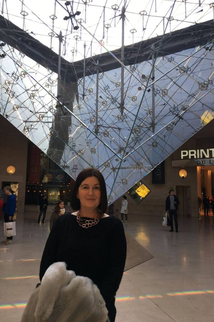 A woman wearing a black jumper and holding a coat stood under the glass ceiling in the Louvre in Paris