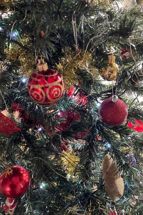 A green Christmas tree decorated with red shiny baubles and gold tinsel