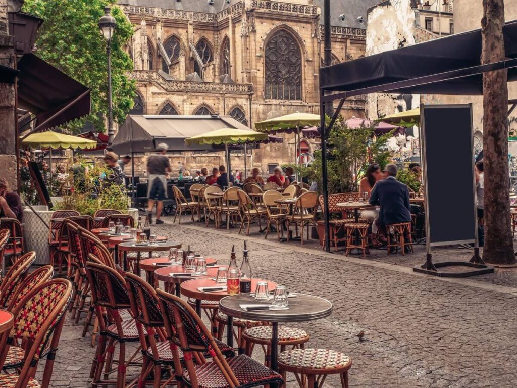 A Parisian cafe with bistro tables and chairs outside with red and white checked tablecloths in front of an old gothic church