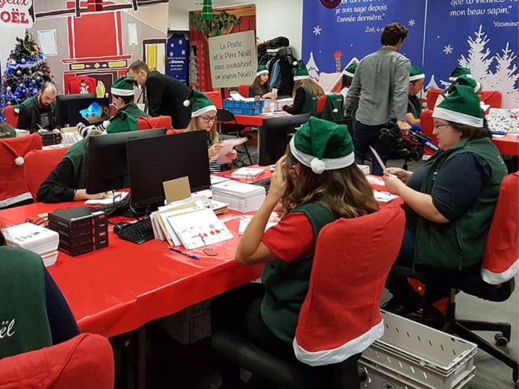 A group of workers dressed in Santa hats working and sorting through letters addressed to Pere Noel