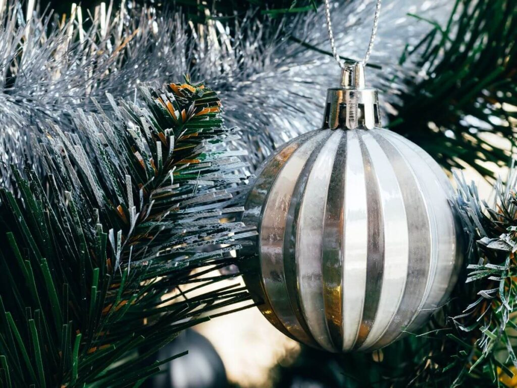 A big silver bauble with silver tinsel hanging from a Christmas Tree