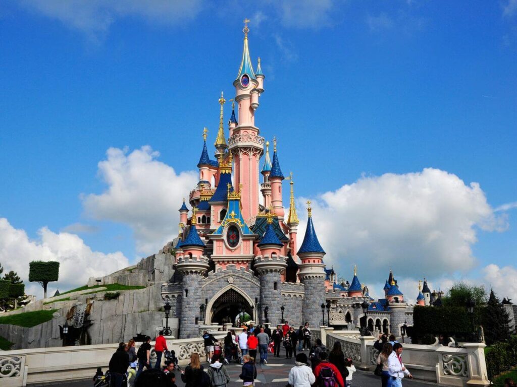 The entrance to Disneyland Paris which is a tall pink tower with people milling around and a blue sky behind