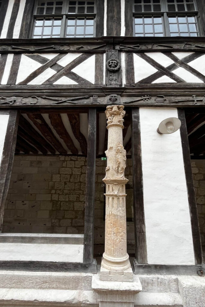 Close-up of a decorative stone column with sculptural details, located at the Saint-Maclou Ossuary in Rouen. The column showcases Gothic craftsmanship, with a series of small figures and ornamental elements that highlight the medieval ecclesiastical architecture of the period.