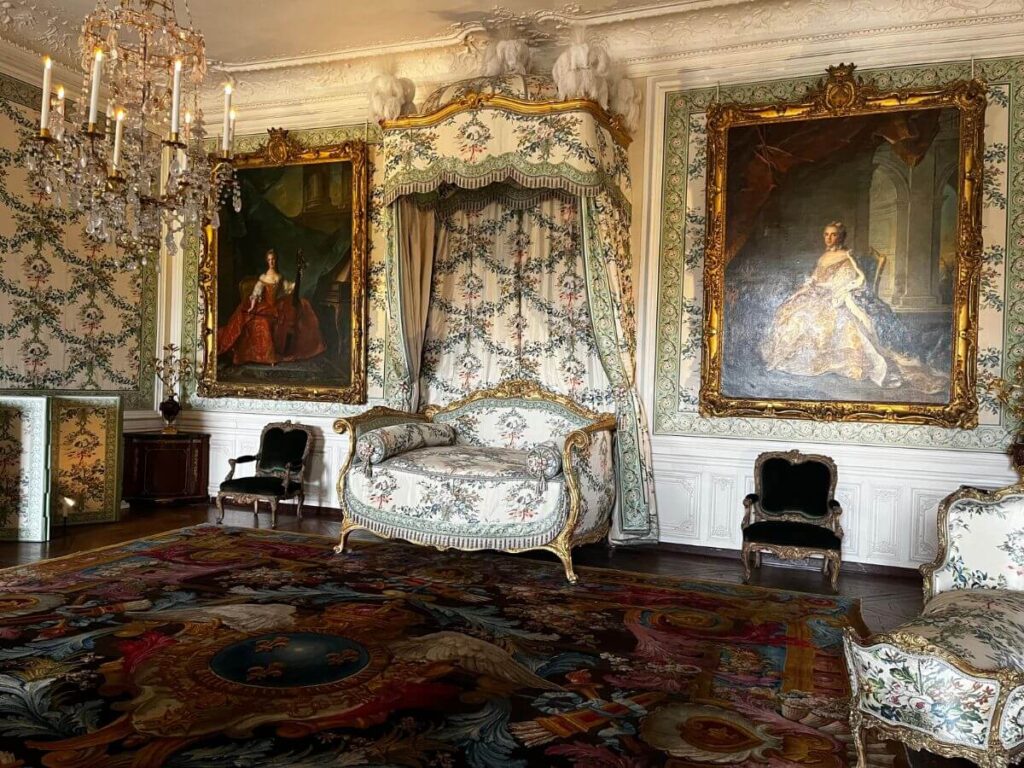 Opulent interior of a Parisian historic attraction featuring ornate Rococo-style furniture, lavish chandeliers, and large portraits in gilded frames.