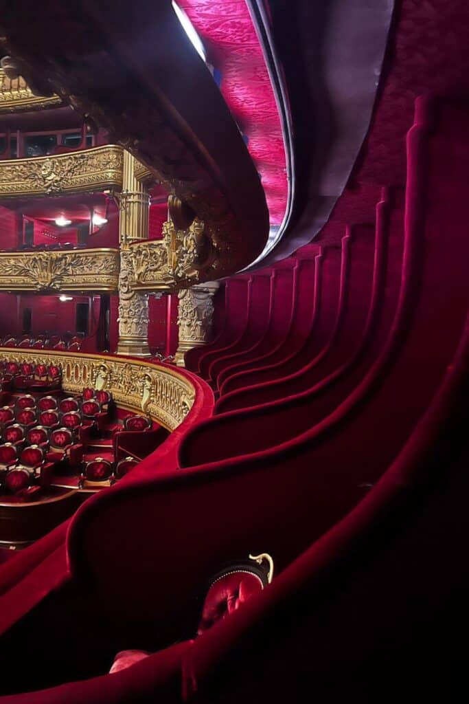 A sweeping view of the rich, red velvet seating and ornate golden balconies inside the Palais Garnier. This perspective, possibly from Box Number 5, alludes to its association with "The Phantom of the Opera," adding a layer of mystique to the theater's historic ambiance.