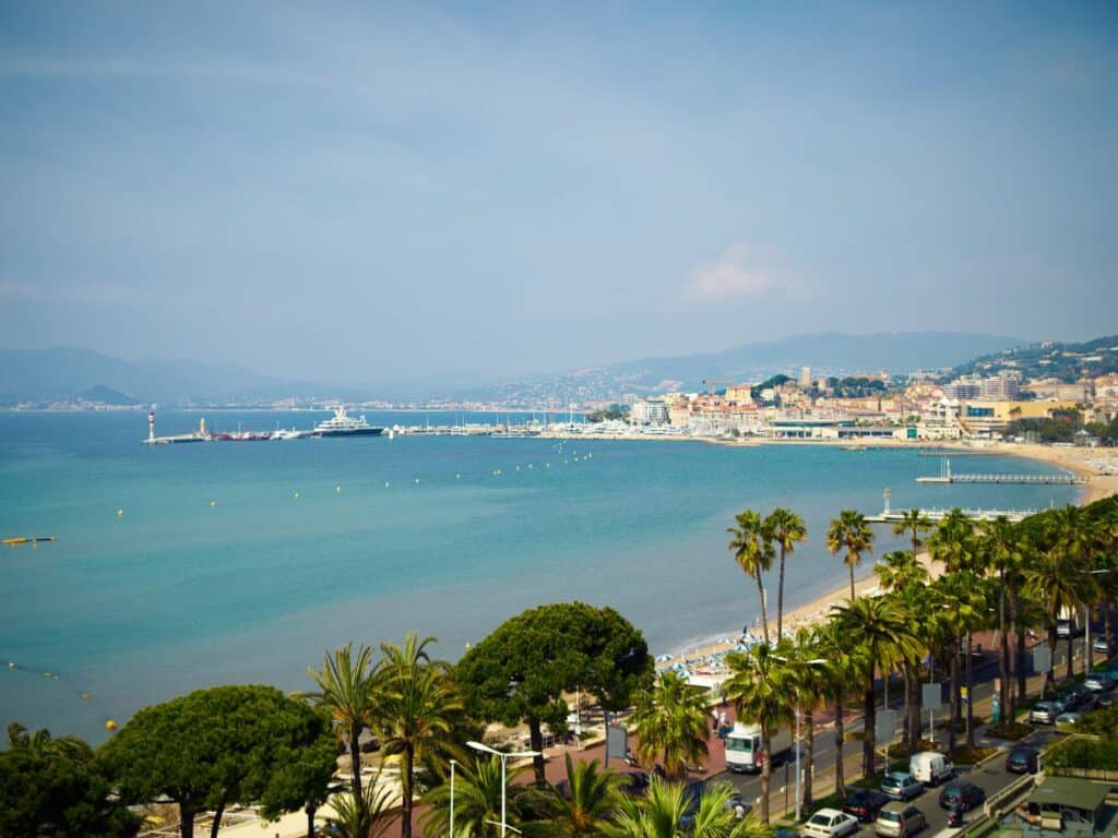 GPT
A panoramic view of the French Riviera, featuring the azure waters of the Mediterranean Sea, a bustling promenade lined with palm trees, and a backdrop of the city of Cannes with its mix of modern and traditional architecture under a hazy blue sky.