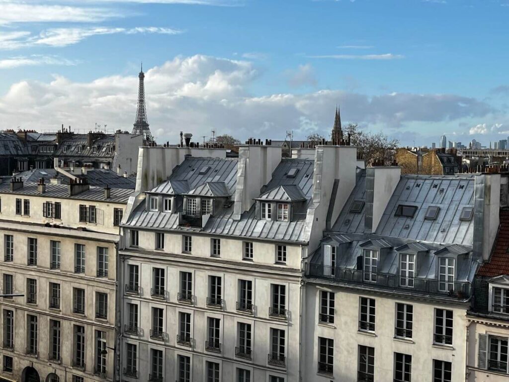 View of Parisian rooftops with the Eiffel Tower in the background under a blue sky with scattered clouds.