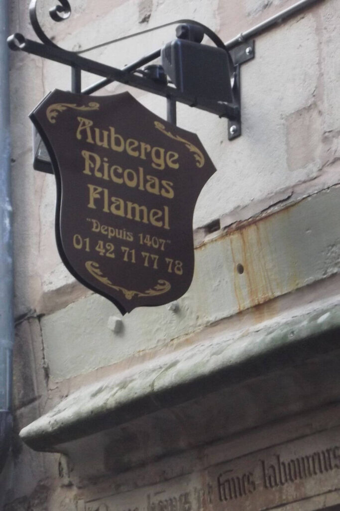 Close-up of the Auberge Nicolas Flamel sign, a historic establishment since 1407, affixed to a stone wall in Paris with elegant golden script.