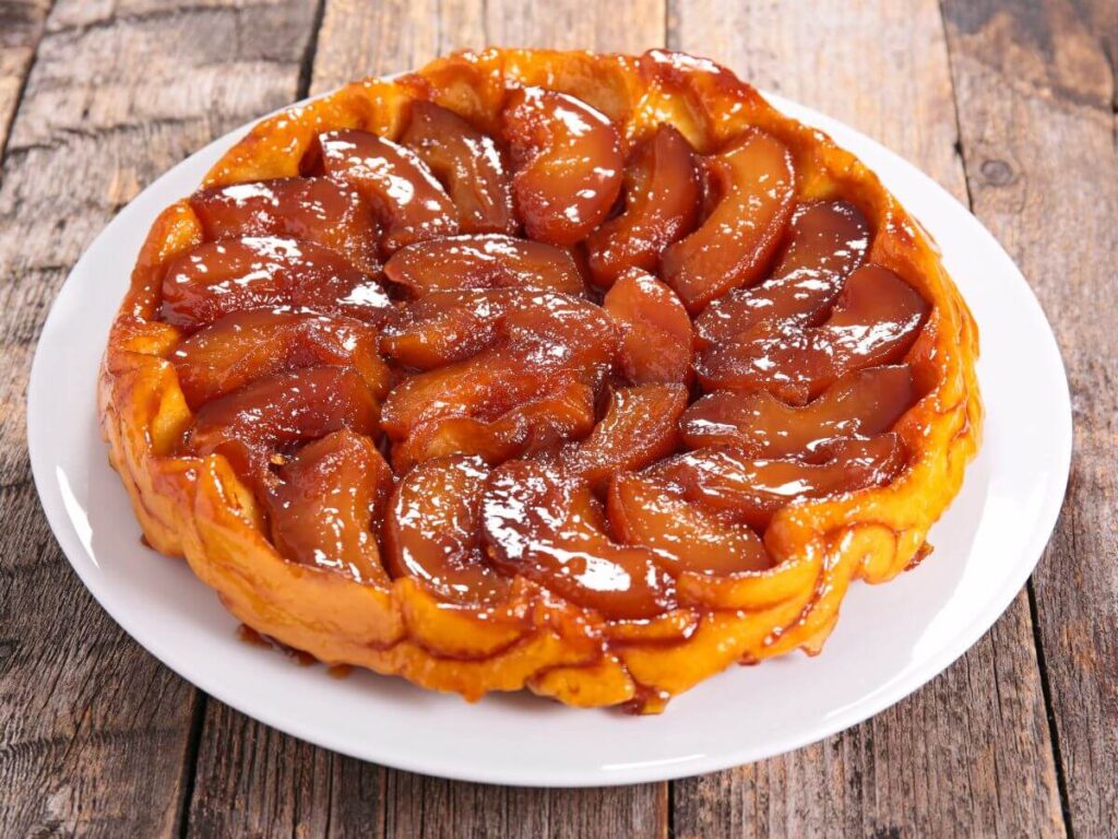 Classic Tarte Tatin displayed on a white plate, featuring caramelized apples with a glossy finish, on a rustic wooden table background.