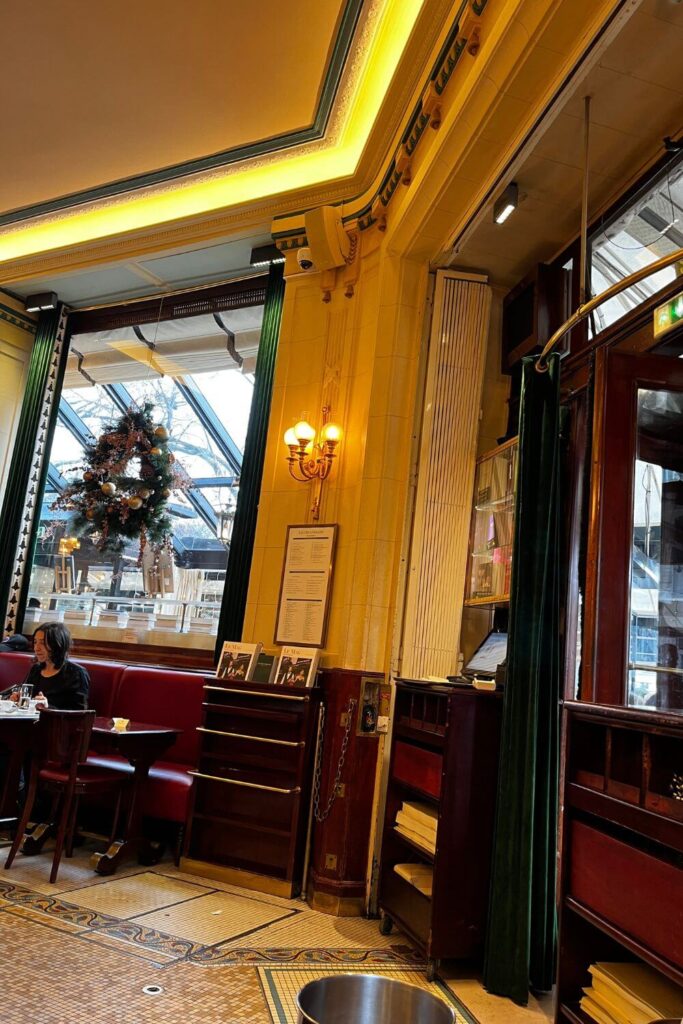 Cozy corner inside Les Deux Magots café with red seating, ambient lighting, and large windows offering a glimpse of the Parisian streets, reflecting the café's rich artistic history.
