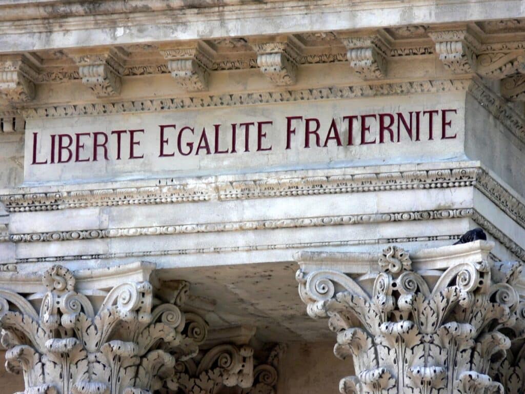 Close-up of an ornate stone frieze inscribed with 'LIBERTE EGALITE FRATERNITE' in red letters, the national motto of France, representing freedom, equality, and brotherhood. The detailed Corinthian column capitals add to the historical significance of the architecture.