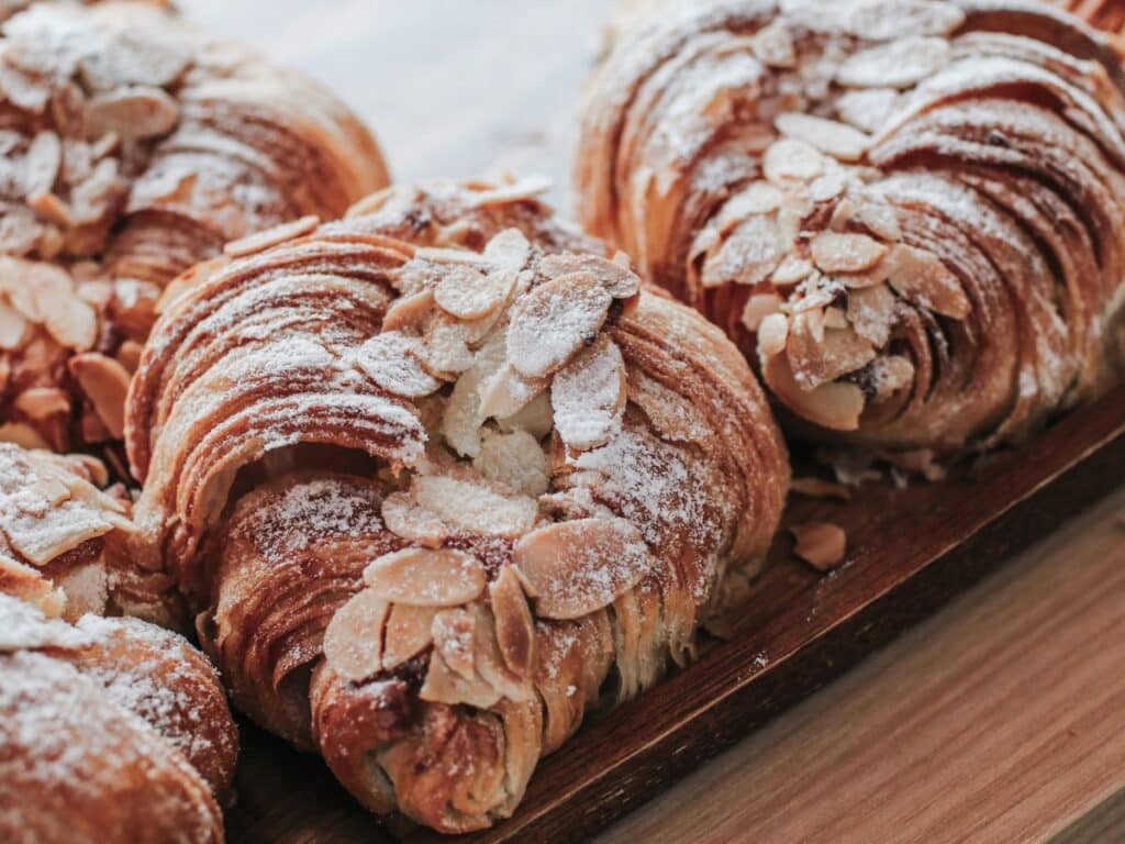 Close-up of almond croissants with a generous topping of sliced almonds and dusted with powdered sugar, served on a wooden platter.