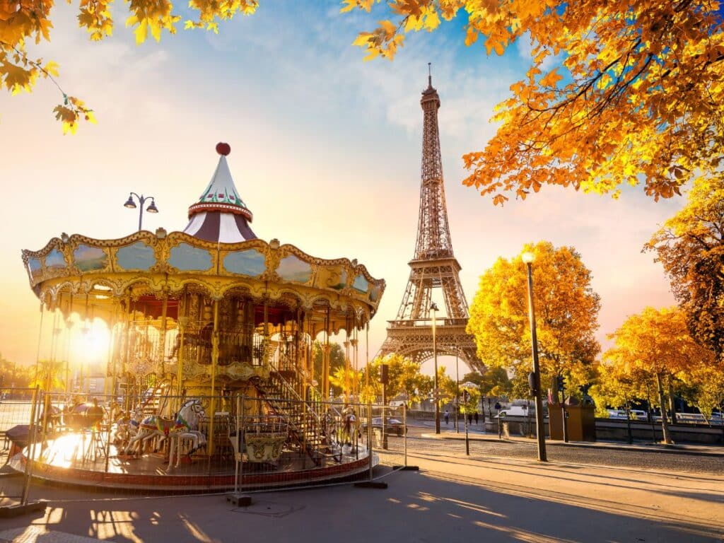 Autumn leaves frame the Eiffel Tower behind a classic carousel in golden hour light.