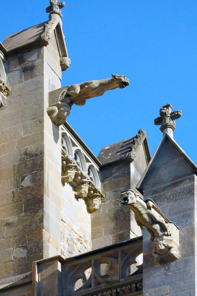 Close-up of the intricate gargoyles and Gothic architectural details on the exterior of the Carcassonne Cathedral, set against a vivid blue sky.