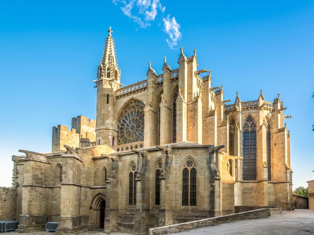 Exterior view of the Carcassonne Cathedral, also known as the Basilica of St. Nazaire, showcasing its Gothic architectural details, ornate stonework, and the large rose window under a clear blue sky.
