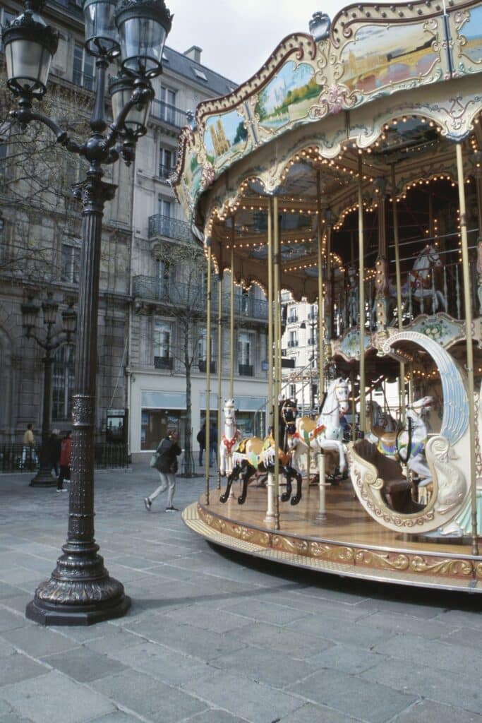 Carousel in Parisian square with surrounding traditional architecture on a cloudy day.