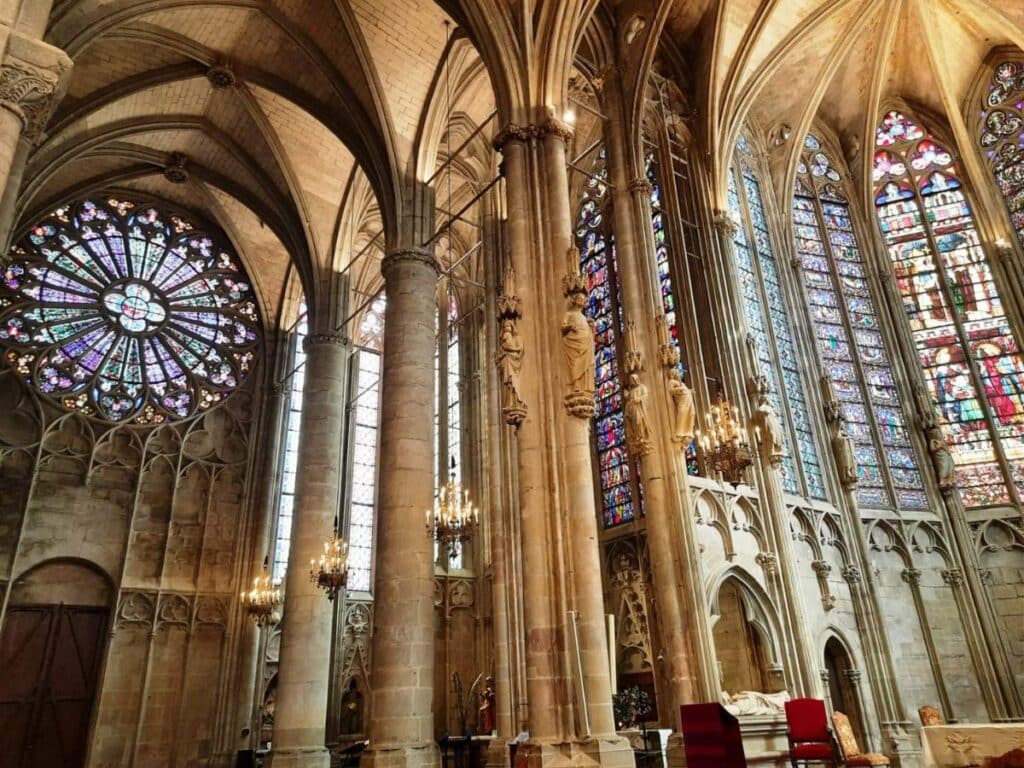 Interior of Saint Michael's Cathedral of Carcassonne, showcasing a large rose window and multiple stained glass panels, with chandeliers and Gothic arches enhancing its medieval charm.