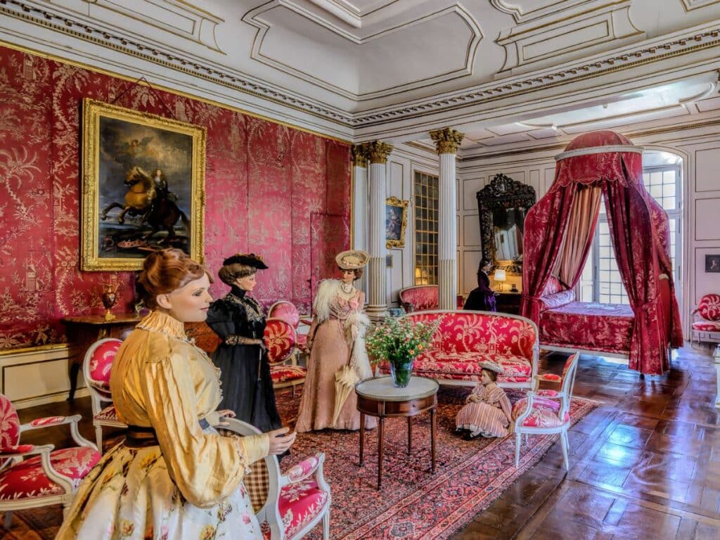 Interior of a luxurious room in Château d’Ussé, Loire Valley, styled with rich red damask wallpaper, period furniture, and mannequins dressed in historical French fashion, an homage to the Disney fairytale of Sleeping Beauty.