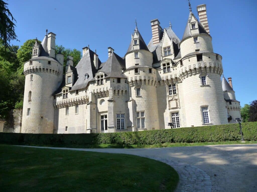 Exterior view of Château d’Ussé in the Loire Valley, a Disney movie location in France with prominent white stone towers and spires, set against a backdrop of lush greenery and clear blue sky.