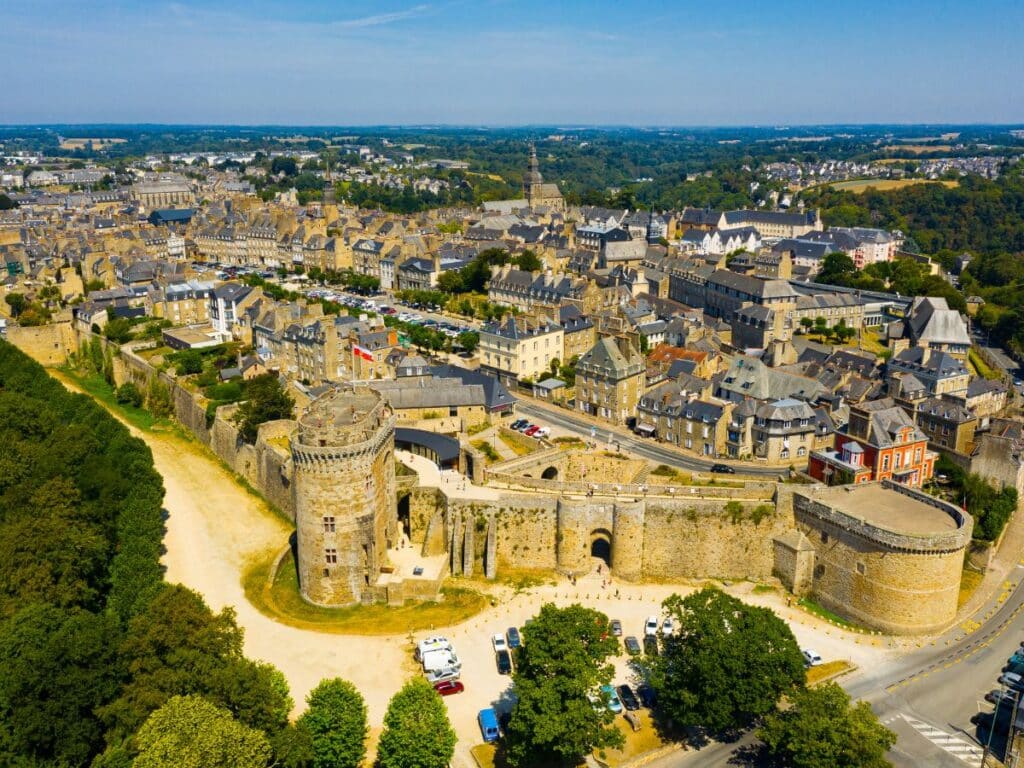Aerial view of the imposing Château de Dinan with its medieval towers and ramparts, surrounded by the dense, historic architecture of Dinan, Brittany, on a sunny day.