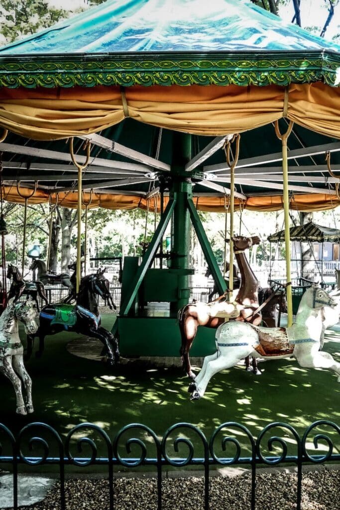 Vintage carousel with faded paint and classic horses under a green canopy in a park.