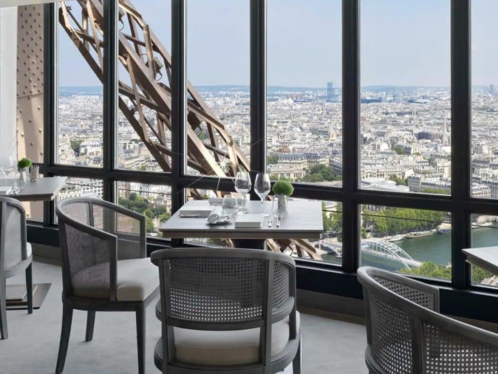 Breathtaking panoramic view from Le Jules Verne restaurant within the Eiffel Tower, featuring a sophisticated dining area with chic furniture and floor-to-ceiling windows overlooking Paris's expansive cityscape.