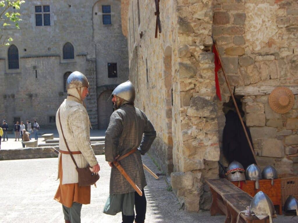 Two actors in medieval costume at Carcassonne Castle, engaging with each other in a cobblestoned courtyard, bringing historical reenactments to life for special events.