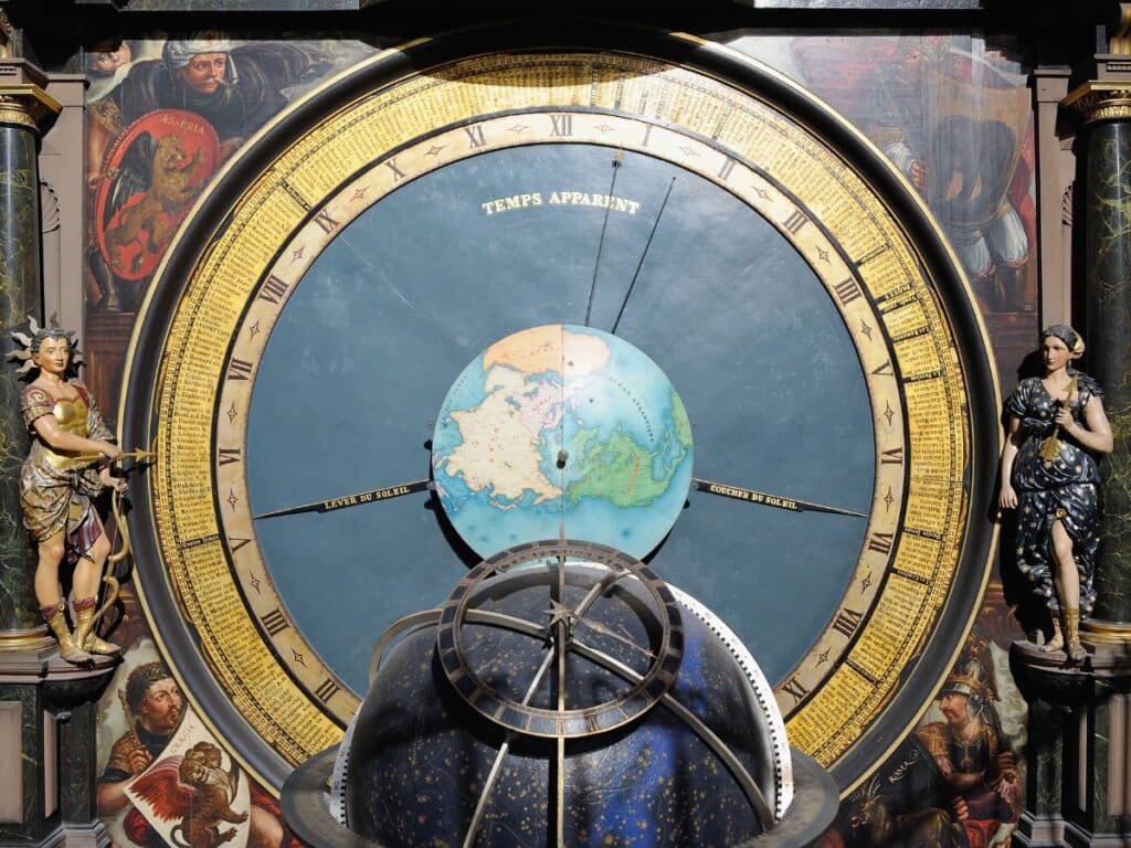 Detailed view of the Strasbourg Astronomical Clock, featuring a large circular dial with Roman numerals, a central terrestrial globe, and elaborate sculptures including figures of a warrior and a draped woman, with ornate paintings in the background.