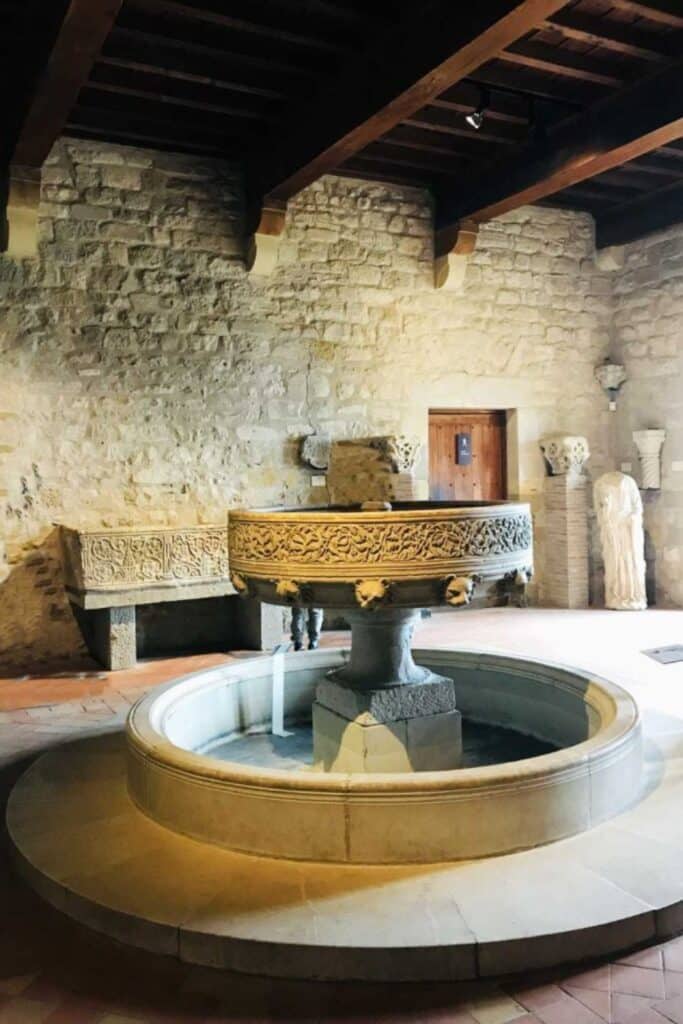 The interior of a room in Carcassonne Castle, with a grand central fountain and intricate stone carvings, reflecting the castle's architectural splendor and inviting visitors on a historical tour.