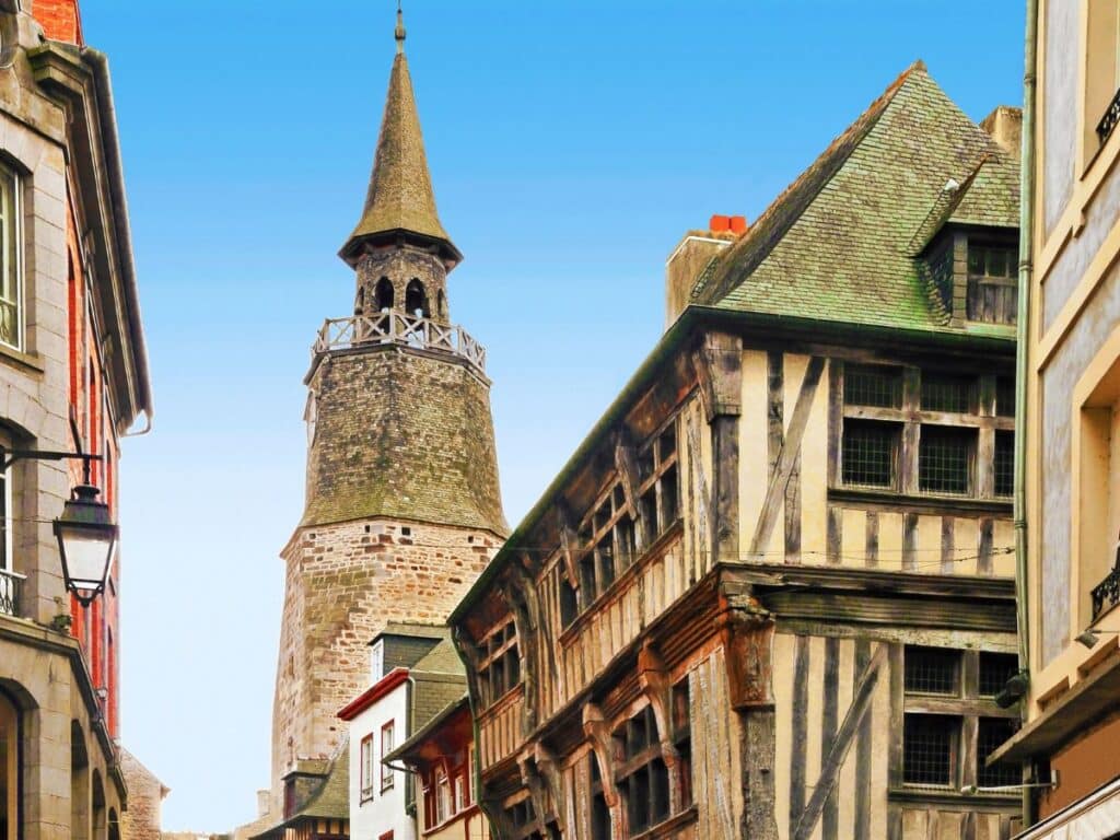 The historic Clock Tower (Tour de l'Horloge) in Dinan, Brittany, peeks above timber-framed houses lining the narrow street, blending medieval architecture with urban charm.
