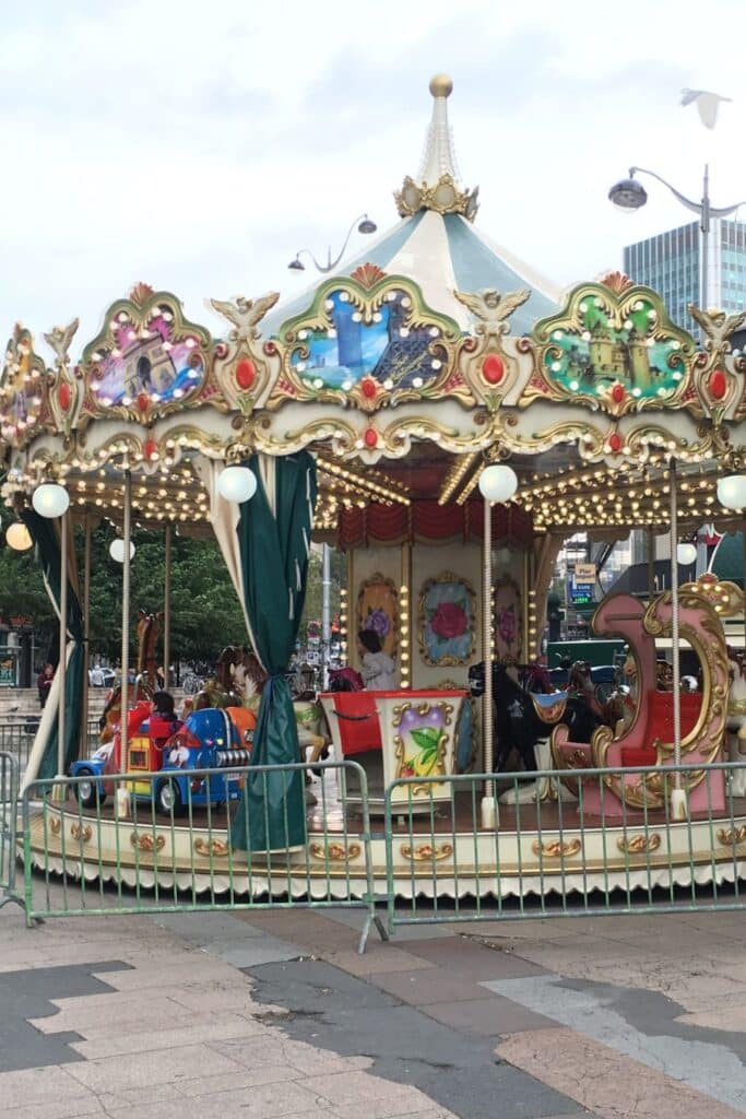 Colorful carousel with gold embellishments and festive lights in an urban setting.