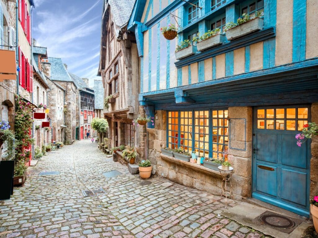 Cobblestone street lined with colorful half-timbered houses and blooming flower pots in a quaint Brittany village, showcasing vibrant architectural charm and inviting atmosphere.
