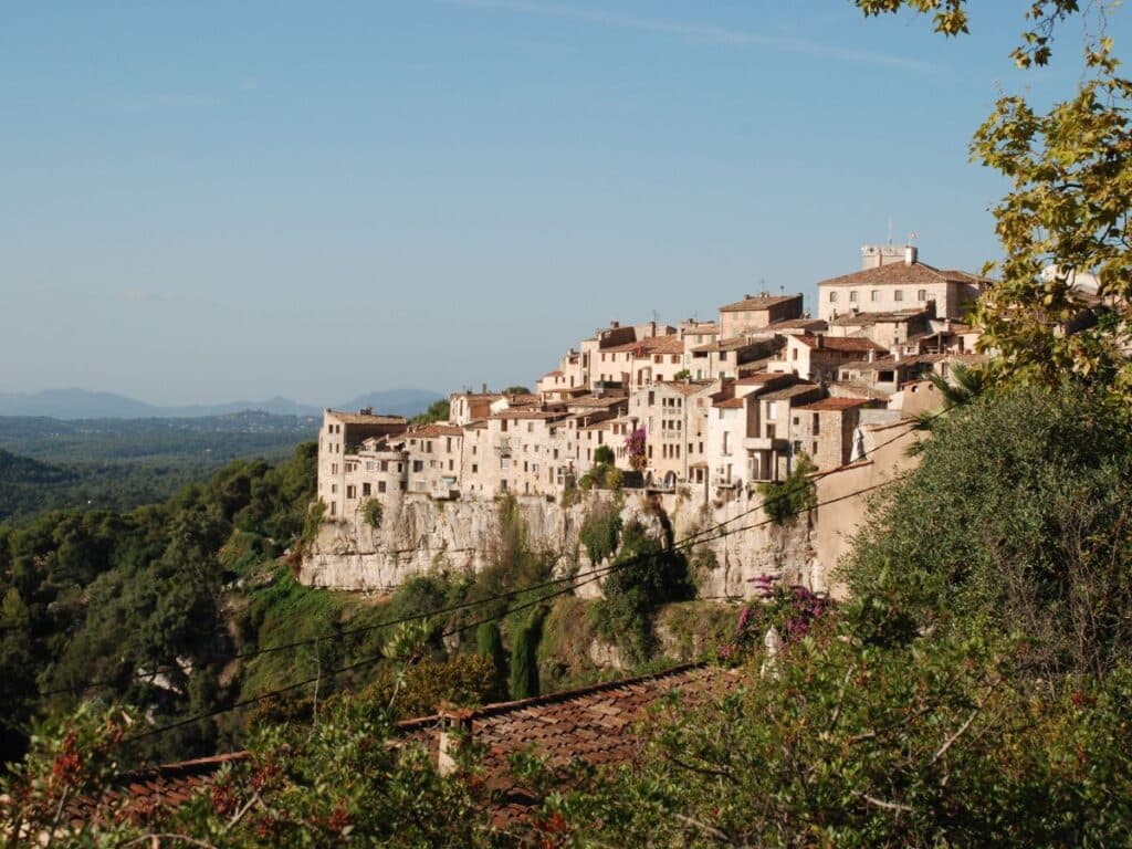 Panoramic view of Tourrettes-sur-Loup village perched on a cliff under a clear sky.
