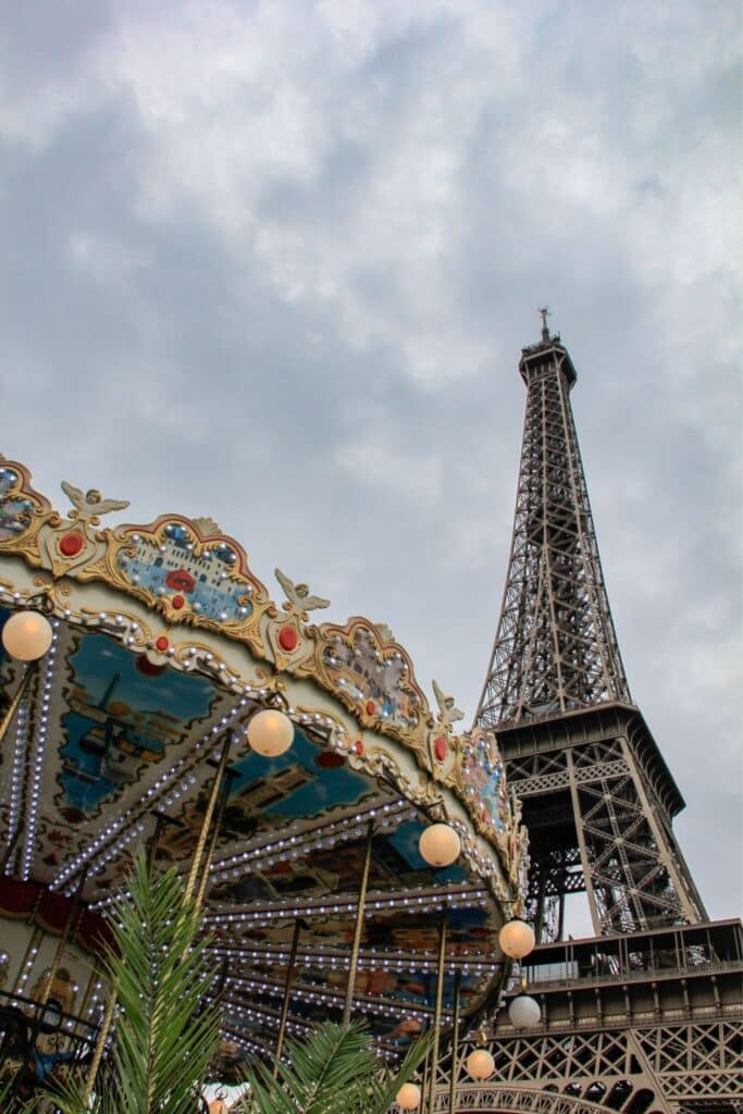 Majestic Eiffel Tower looms over an ornate carousel adorned with lights and artwork.