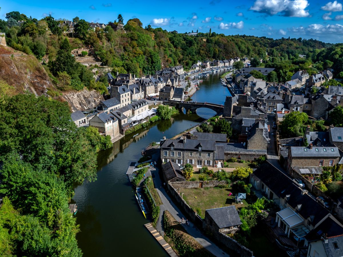A panoramic view of Dinan's medieval town, showing a winding river, stone houses, and lush green hills, with the vibrant charm of this hidden gem in Brittany.