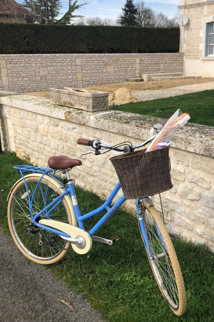 Blue bicycle with a basket of baguettes by a stone wall.