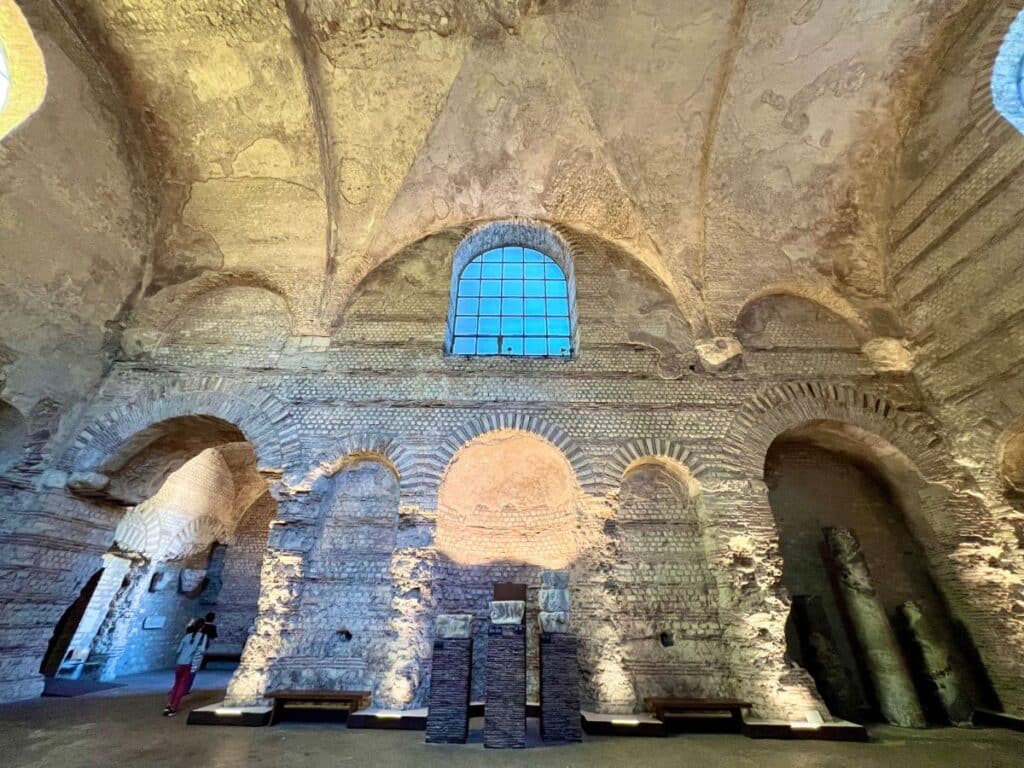 Ancient Roman baths with soaring arches and brickwork, illuminated gently.