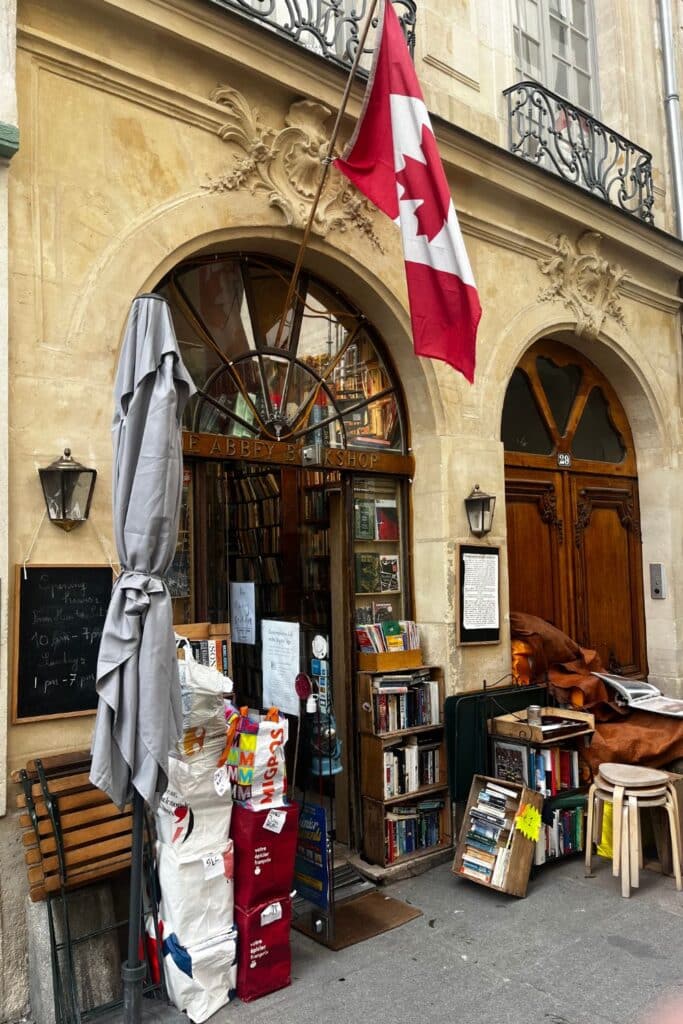 Cozy bookshop facade with a vibrant Canadian flag, a stone arch, and books outside.