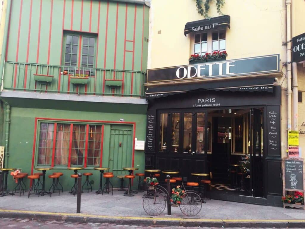 Green Parisian cafe facade with red accents and outdoor seating.