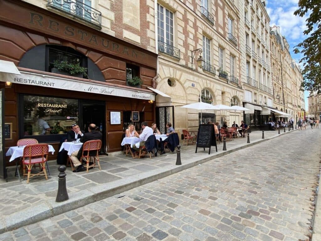 Diners enjoy a meal at a cobbled street-side Parisian café.
