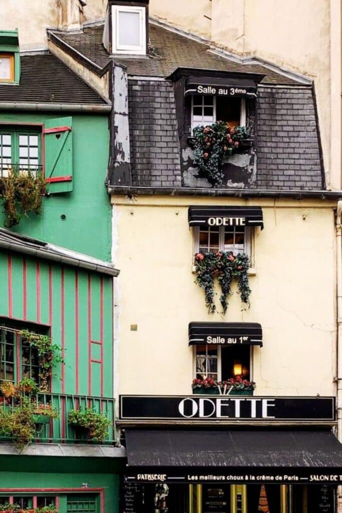 Parisian pastry shop with flowering window boxes, under a clear sky.