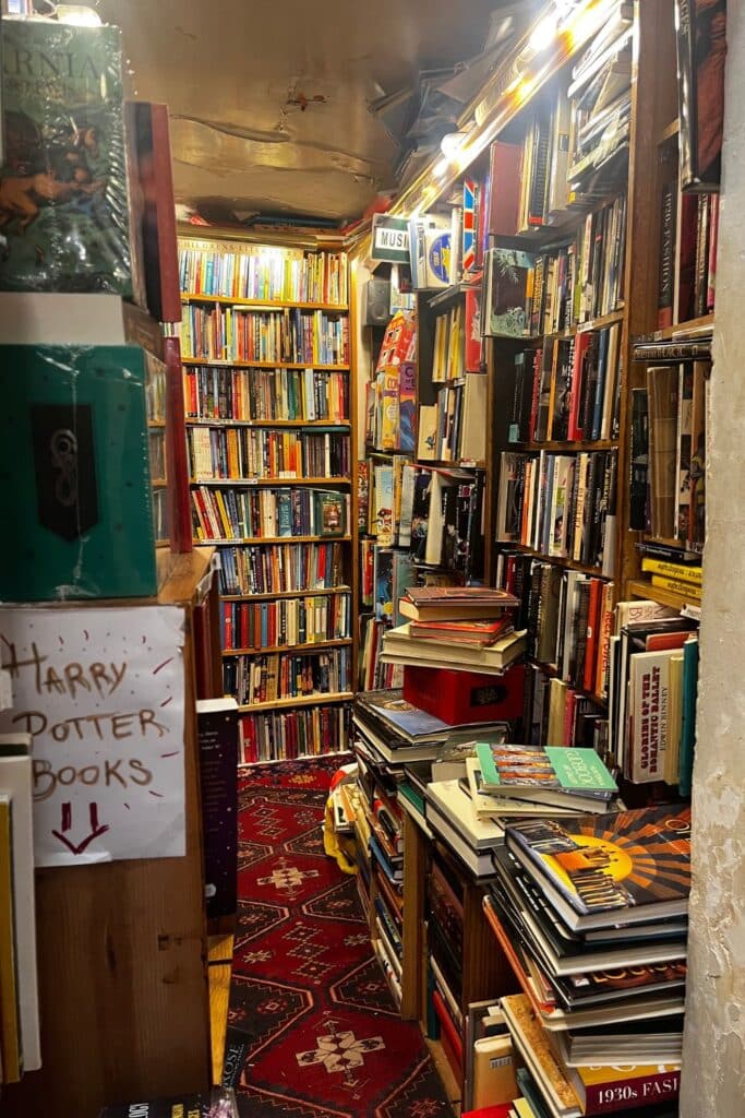 Cozy bookstore aisle with books piled high and a sign for Harry Potter books.