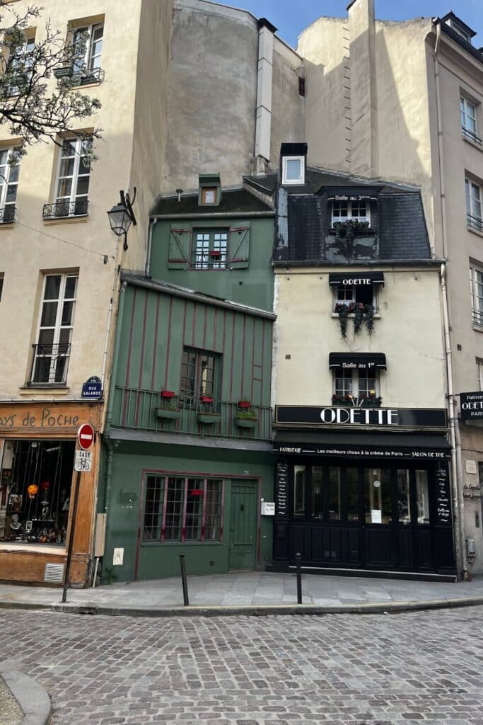 Corner view of a quaint green Parisian cafe, cobbled streets visible.